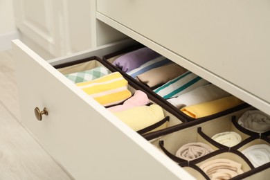 Photo of Organizers with folded clothes in drawer indoors, closeup