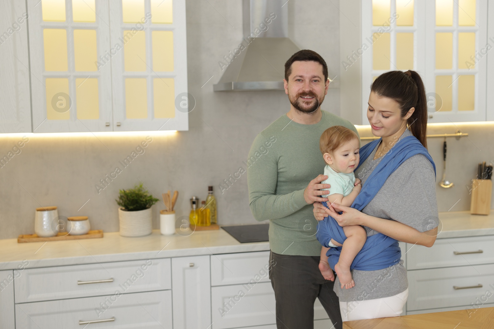 Photo of Portrait of happy family indoors, space for text. Mother holding her child in sling (baby carrier) at home