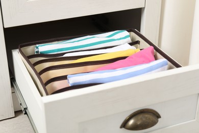 Organizer with folded clothes in drawer indoors, closeup