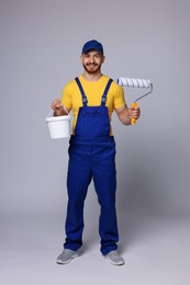 Professional painter with roller and bucket of paint on light grey background