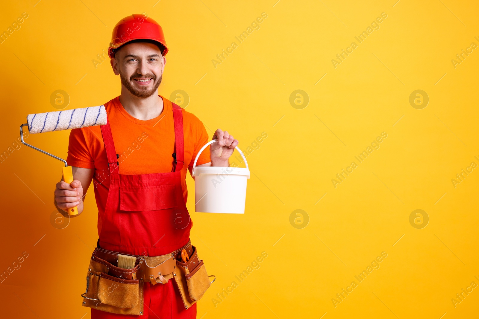 Photo of Professional painter with roller and bucket of paint on orange background. Space for text