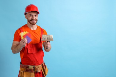 Photo of Professional painter with brush and color samples on light blue background. Space for text