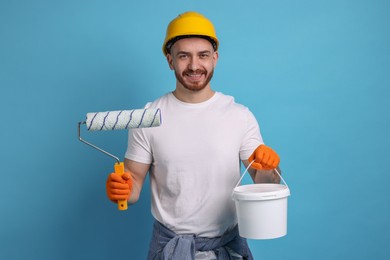 Man wearing hardhat with roller and bucket of paint on blue background