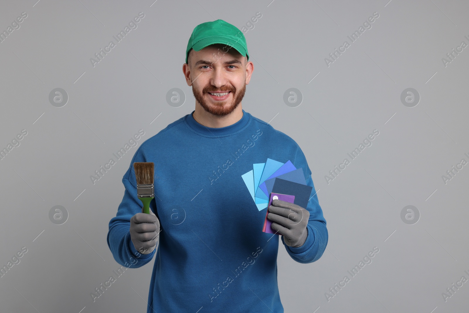 Photo of Man with paintbrush and color samples on light grey background