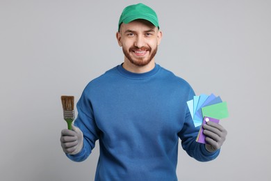 Photo of Man with paintbrush and color samples on light grey background