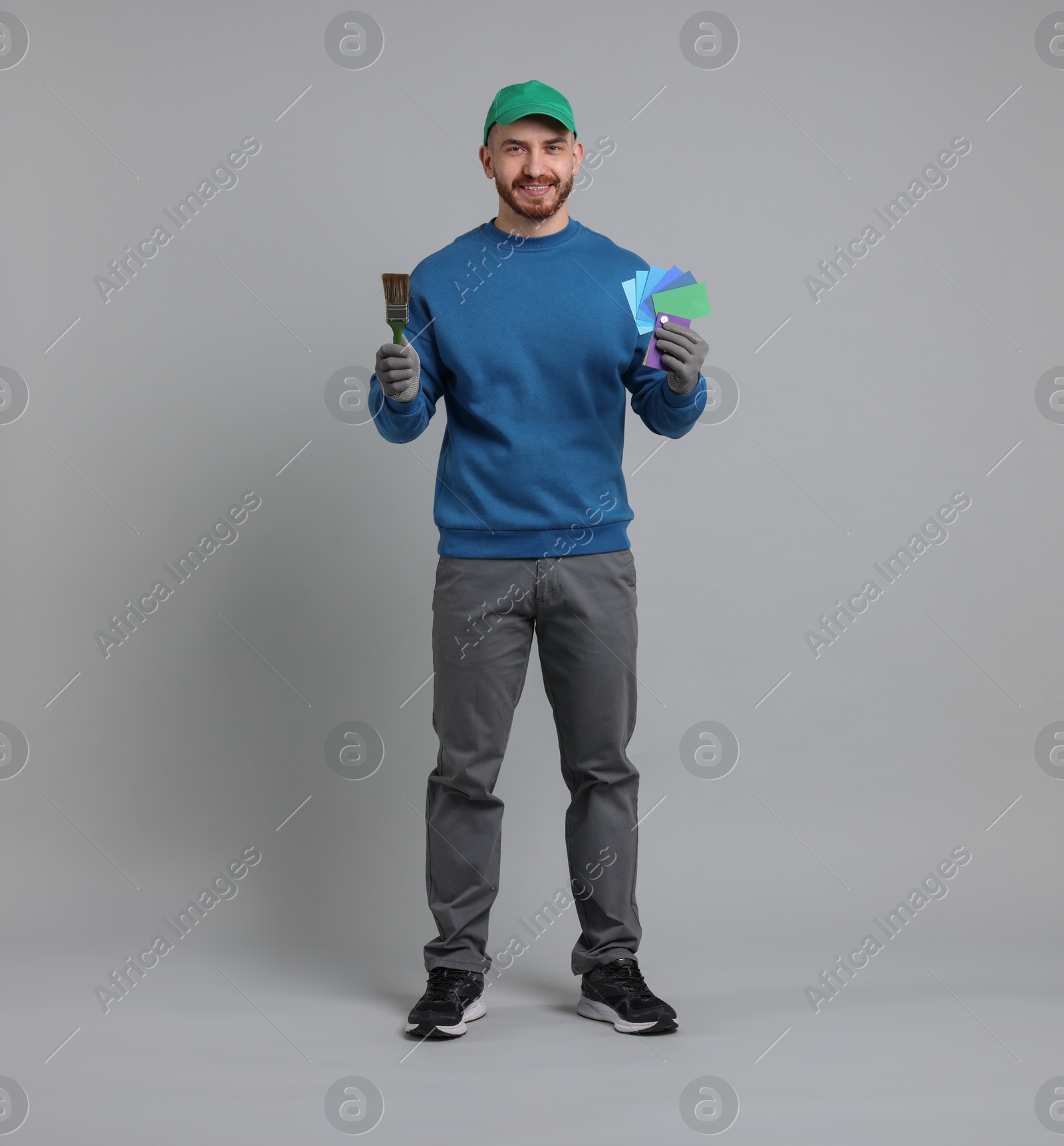 Photo of Man with paintbrush and color samples on light grey background