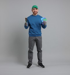 Photo of Man with paintbrush and color samples on light grey background