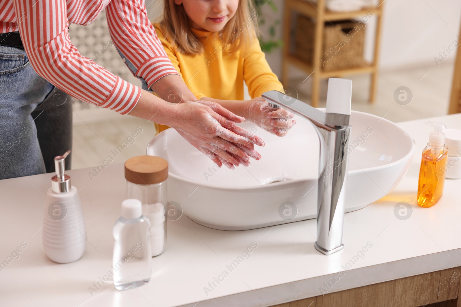 Photo of Mother and daughter washing their hands above sink indoors, closeup