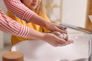 Photo of Mother and daughter washing their hands above sink indoors, closeup