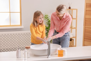 Happy mother and daughter washing their hands in bathroom. Space for text