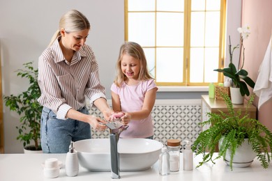 Happy mother and daughter washing their hands in bathroom