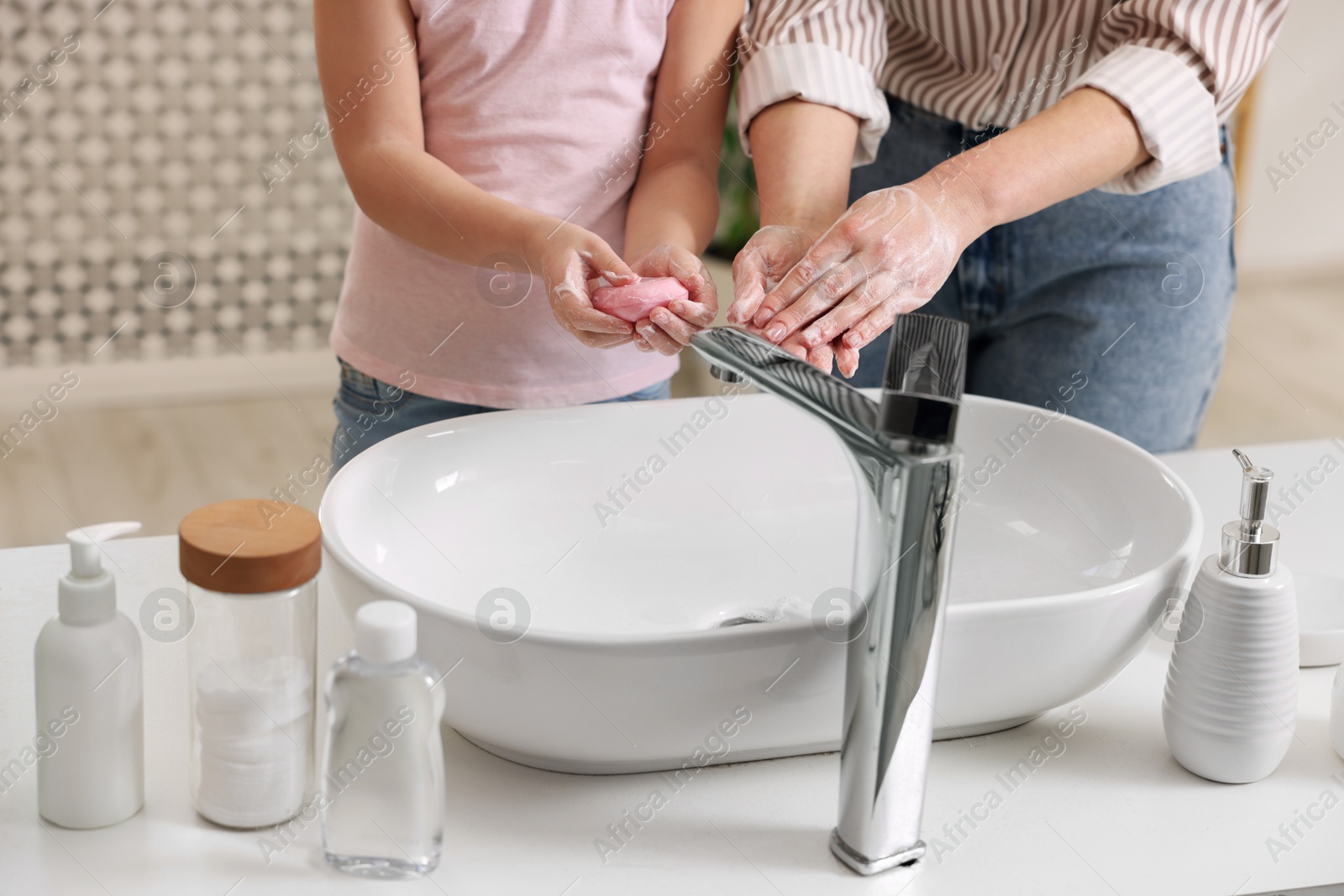 Photo of Mother and daughter washing their hands indoors, closeup