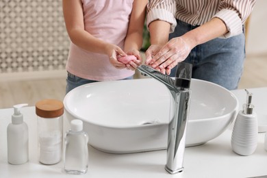 Photo of Mother and daughter washing their hands indoors, closeup