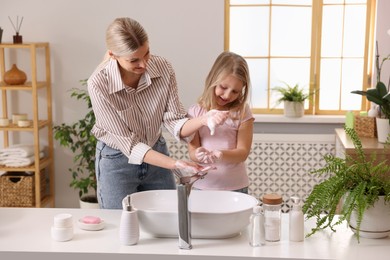 Happy mother and daughter washing their hands in bathroom