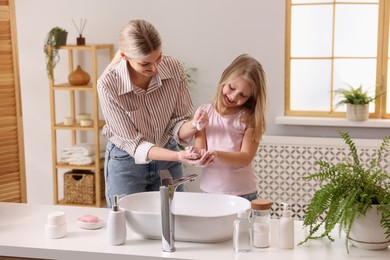 Happy mother and daughter washing their hands in bathroom