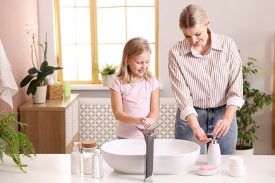 Happy mother and daughter washing their hands in bathroom