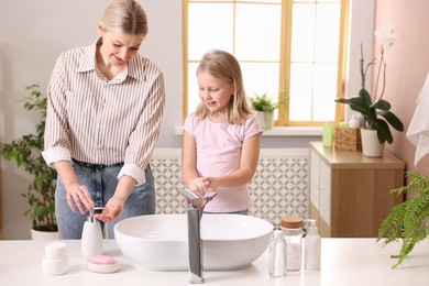 Happy mother and daughter washing their hands in bathroom