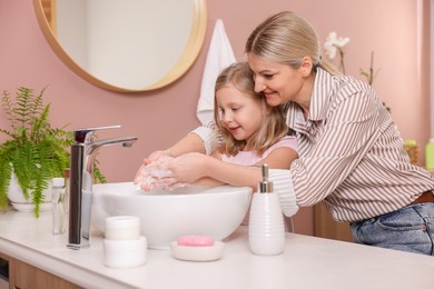 Happy mother and daughter washing their hands in bathroom