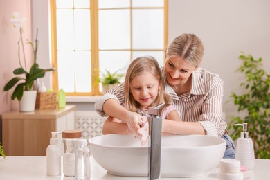 Happy mother and daughter washing their hands in bathroom