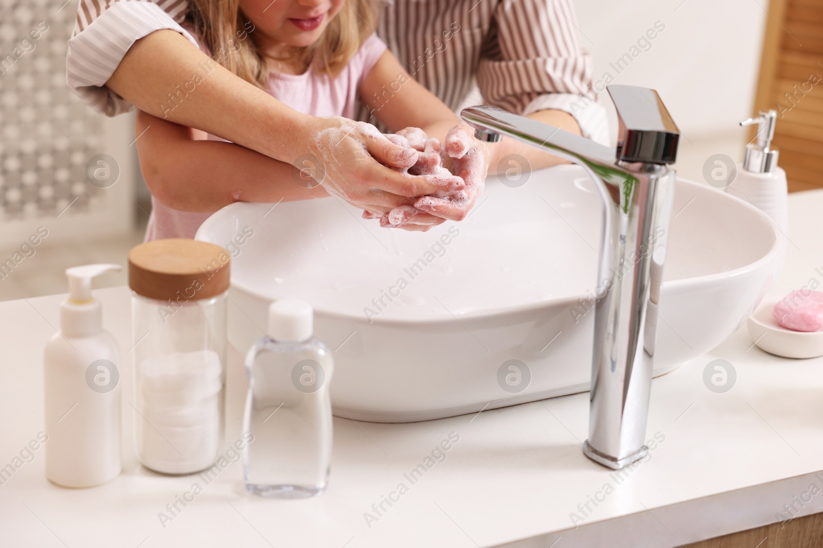 Photo of Mother and daughter washing their hands indoors, closeup