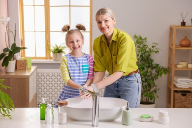 Happy mother and daughter washing their hands in bathroom