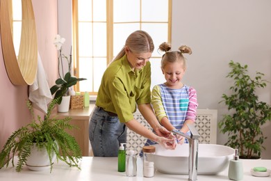 Happy mother and daughter washing their hands in bathroom