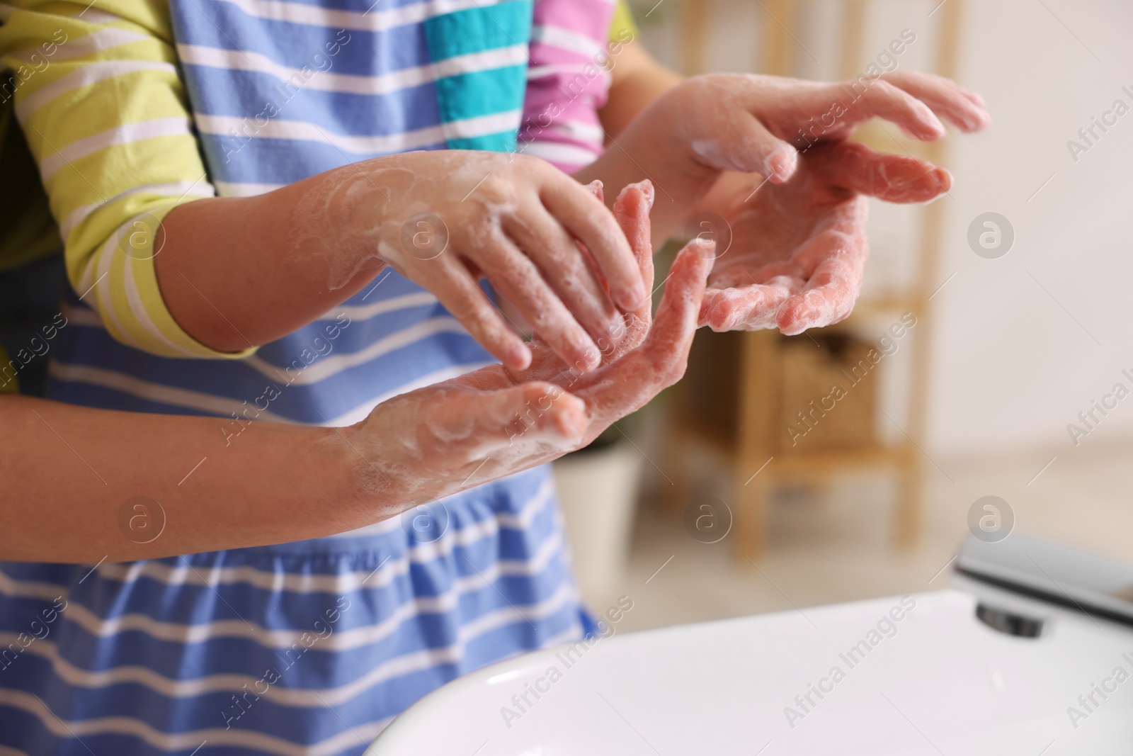 Photo of Mother and daughter washing their hands indoors, closeup