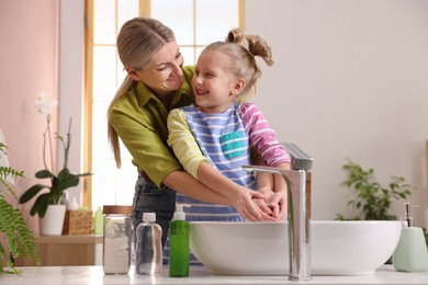 Happy mother and daughter washing their hands in bathroom