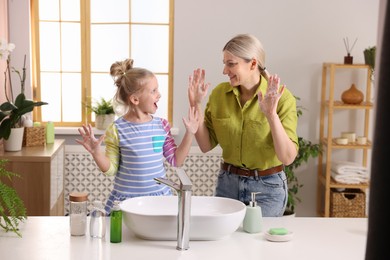 Photo of Happy mother and daughter having fun while washing their hands in bathroom