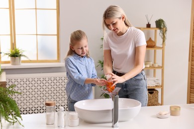 Happy mother and daughter washing their hands in bathroom