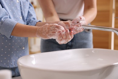 Photo of Mother and daughter washing their hands above sink indoors, closeup