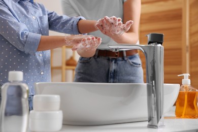 Photo of Mother and daughter washing their hands above sink indoors, closeup