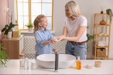 Happy mother and daughter washing their hands in bathroom