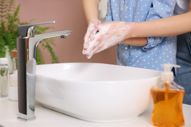 Mother and daughter washing their hands above sink indoors, closeup