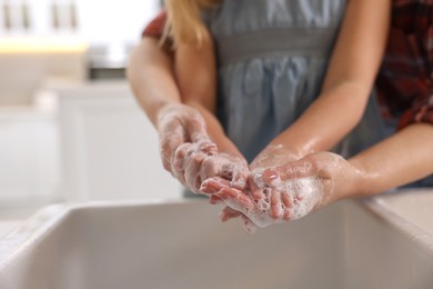 Photo of Mother and daughter washing their hands above sink indoors, closeup. Space for text