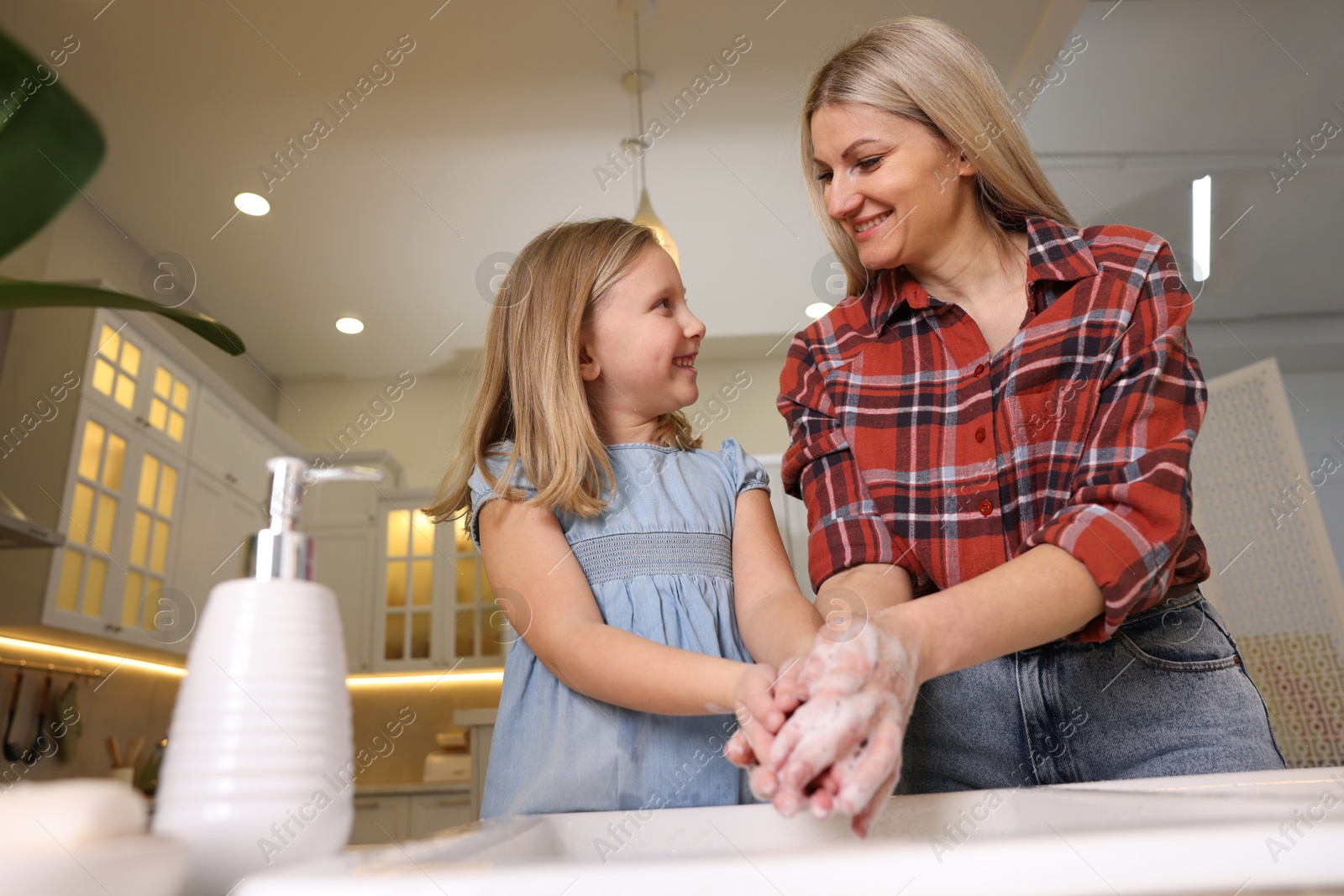 Photo of Happy mother and daughter washing their hands in kitchen, low angle view