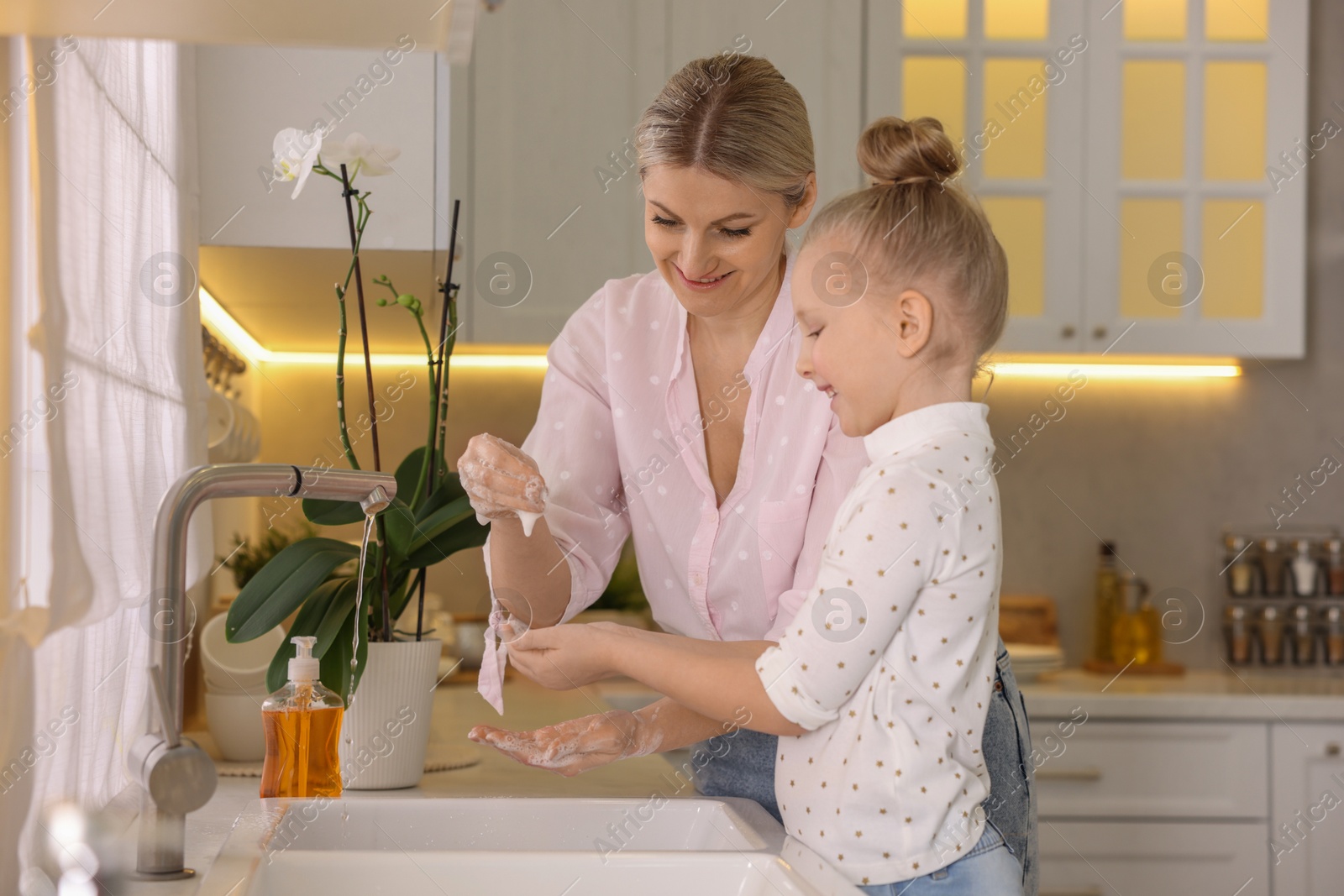 Photo of Happy mother and daughter washing their hands in kitchen