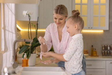 Happy mother and daughter washing their hands in kitchen