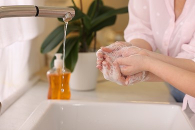 Photo of Mother and daughter washing their hands indoors, closeup