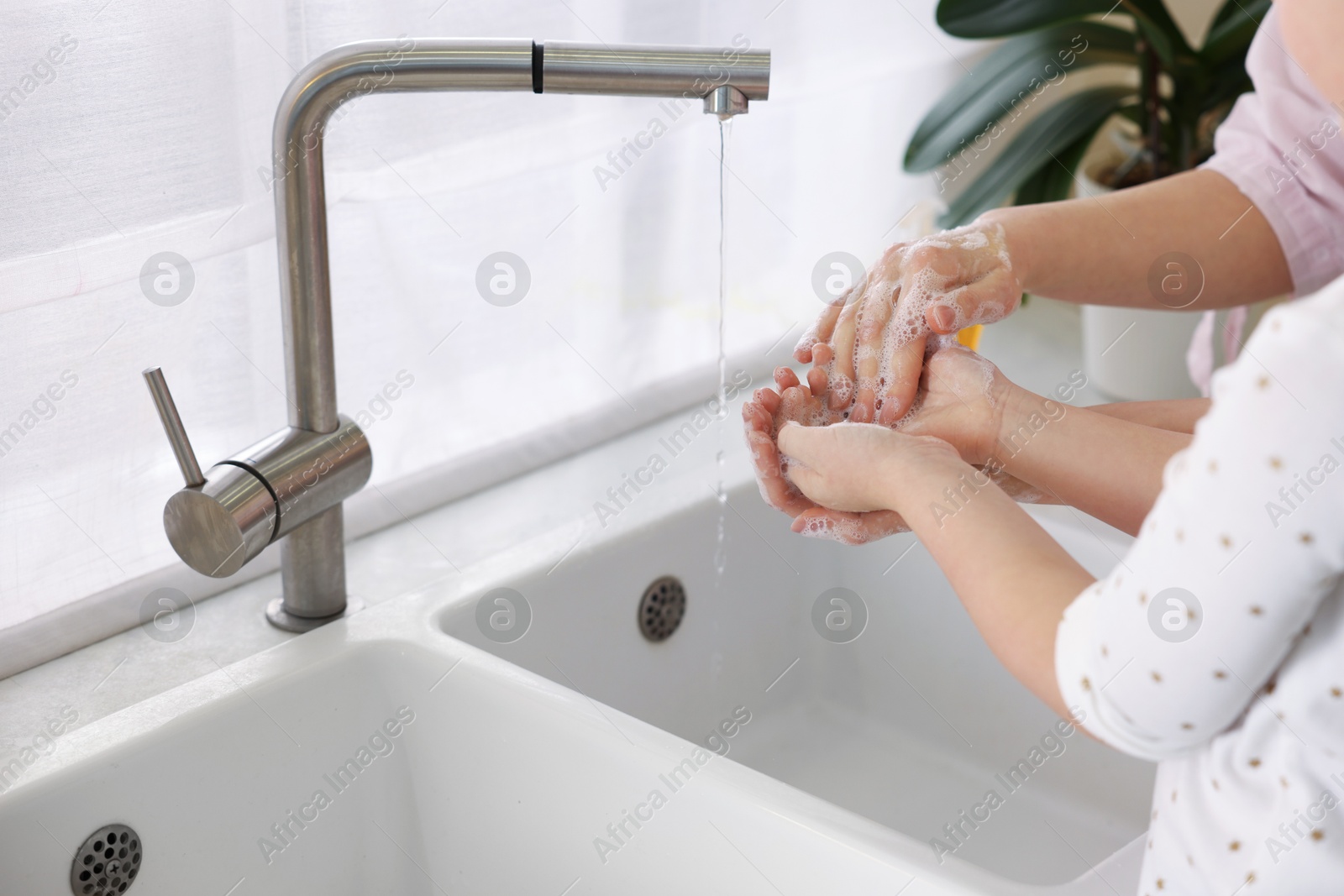 Photo of Mother and daughter washing their hands indoors, closeup