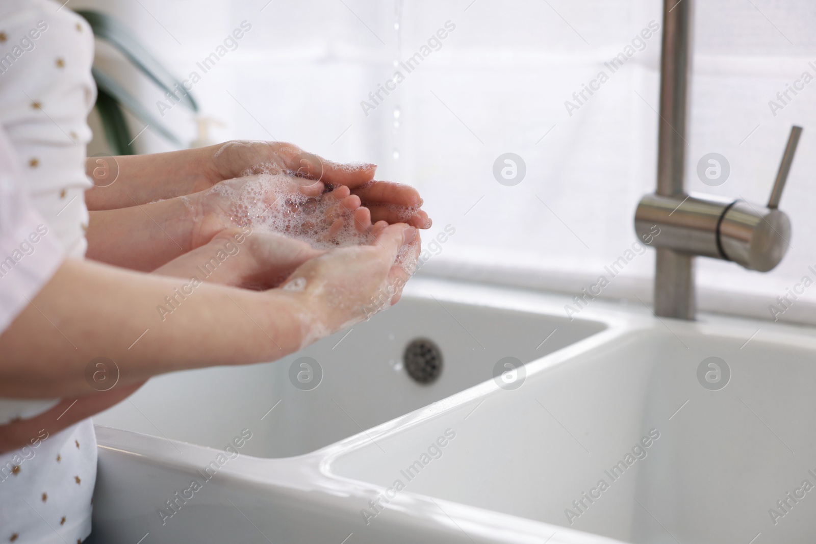 Photo of Mother and daughter washing their hands indoors, closeup. Space for text