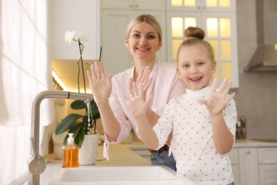 Happy mother and daughter washing their hands in kitchen