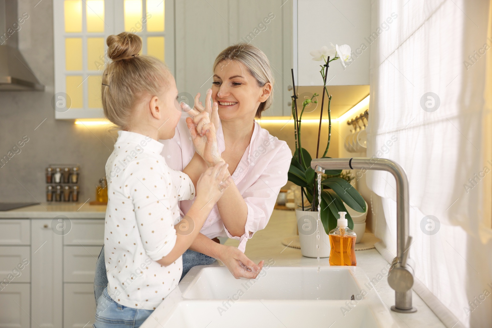 Photo of Happy mother and daughter washing their hands in kitchen