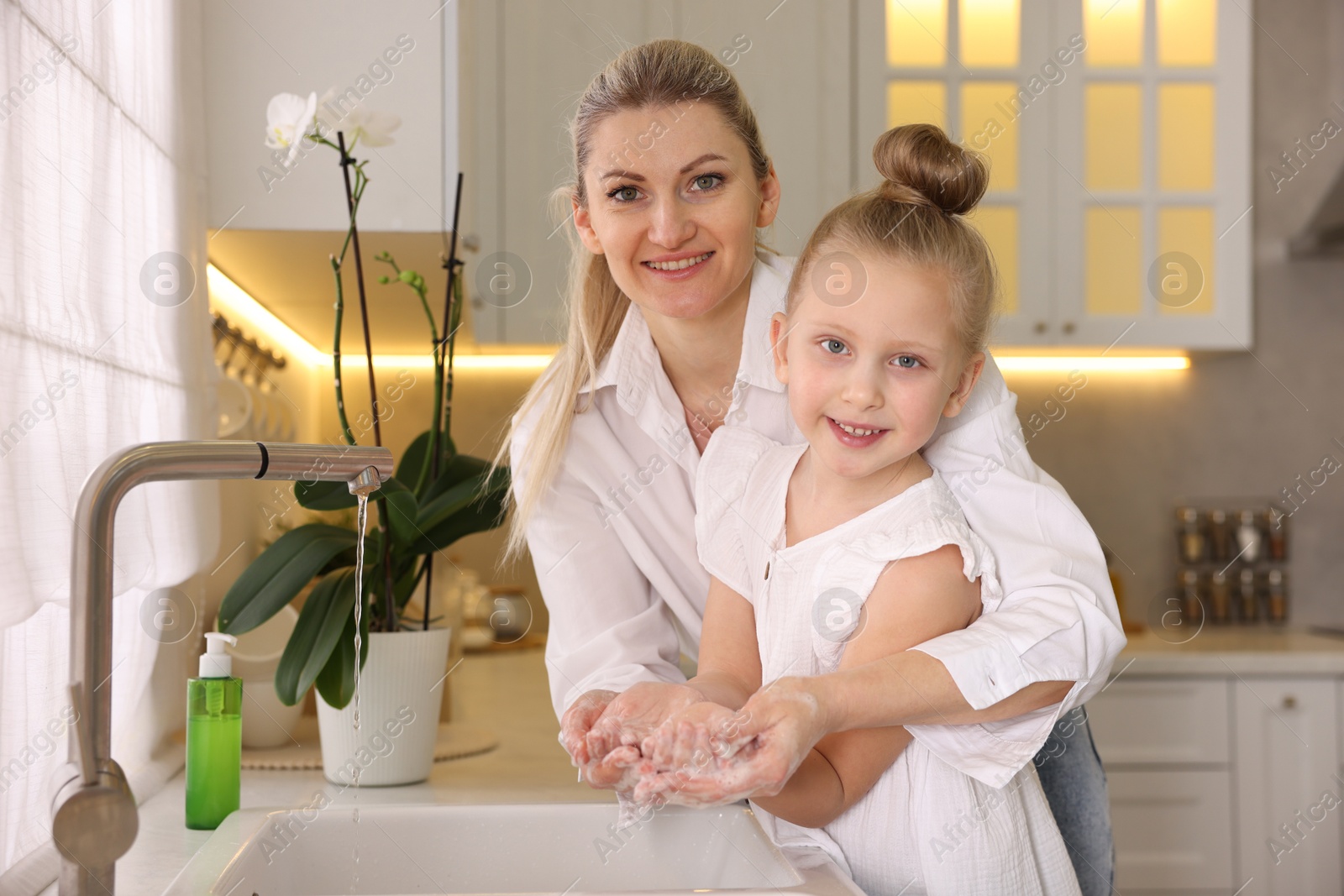 Photo of Happy mother and daughter washing their hands in kitchen