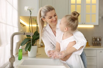 Photo of Happy mother and daughter washing their hands in kitchen