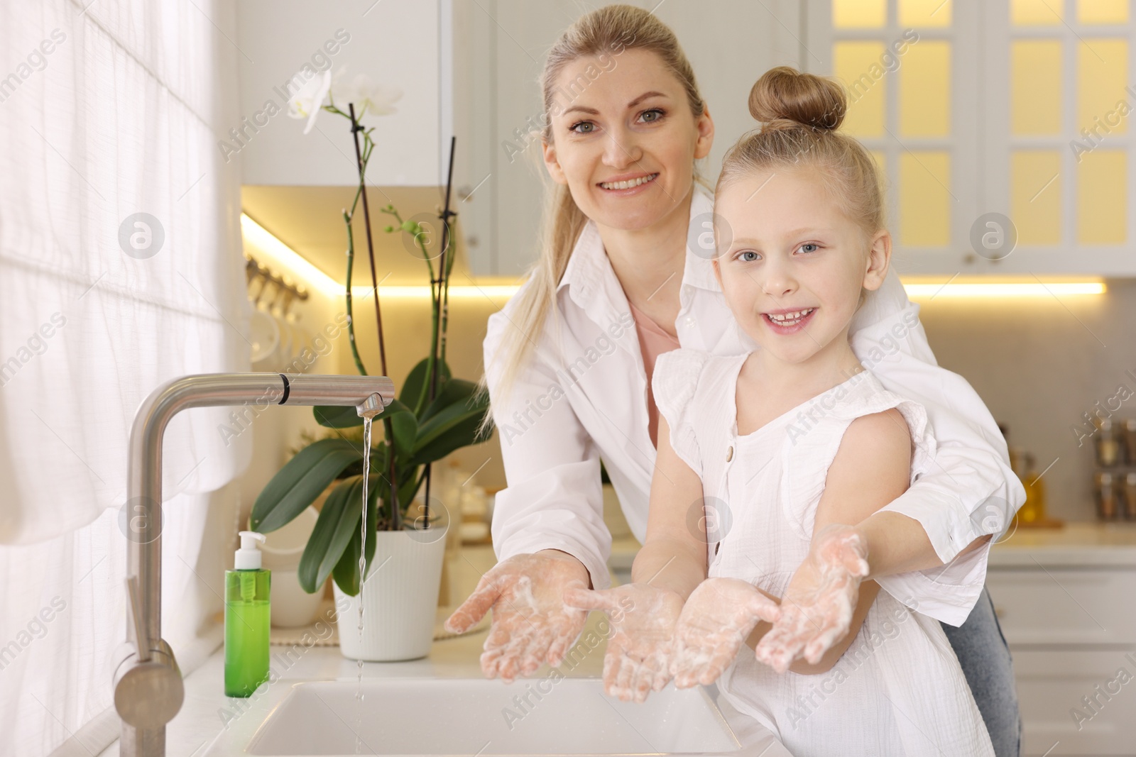 Photo of Happy mother and daughter washing their hands in kitchen