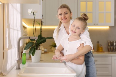 Photo of Happy mother and daughter washing their hands in kitchen