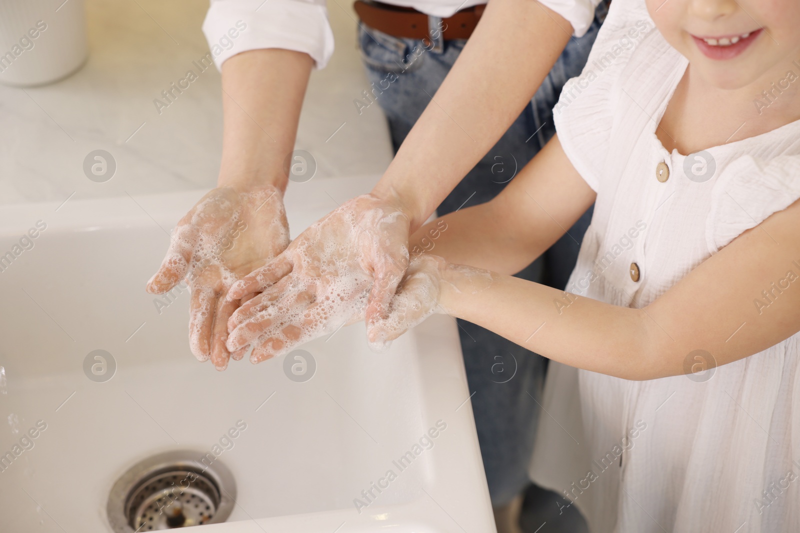 Photo of Mother and daughter washing their hands indoors, closeup