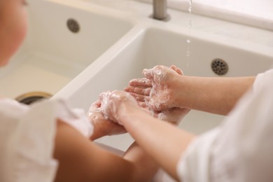 Mother and daughter washing their hands indoors, closeup