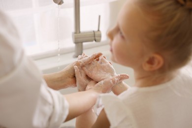 Photo of Mother and daughter washing their hands indoors, closeup